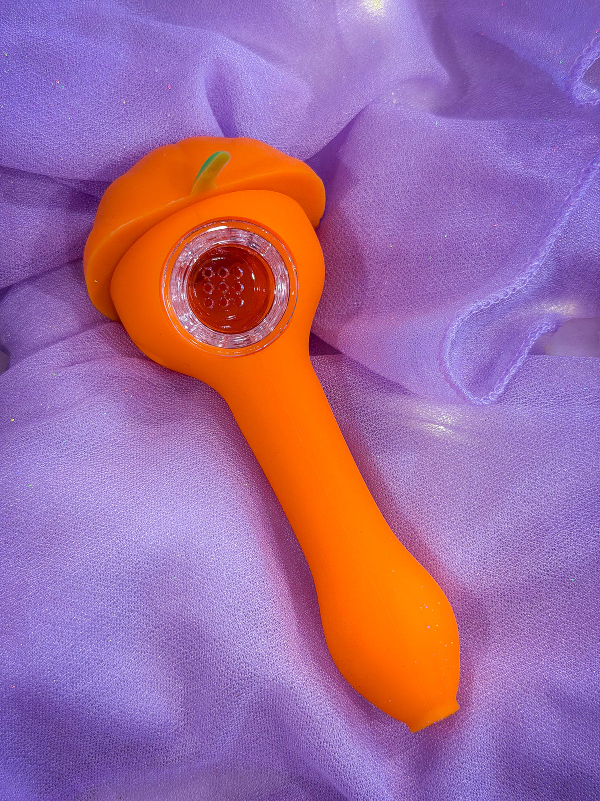 An orange pumpkin silicone pipe and a clear glass bowl, resting on a purple tulle fabric background.